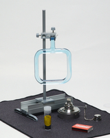 Auf dem Bild sind verschiedene Laborgeräte für Experimente abgebildet, darunter ein Halter mit einer quadratischen Glasschale, ein Reagenzglas mit gelber Flüssigkeit, ein Heizgerät und ein Streichholzheftchen. Diese Materialien sind auf einer dunklen Unterlage angeordnet und eignen sich für chemische Experimente im Bildungsbereich.