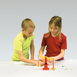 Das Bild zeigt zwei Kinder, die gemeinsam an einer Tischwaage experimentieren. Auf dem Tisch liegen verschiedene kleine Objekte, und die Kinder scheinen die Gewichte zu vergleichen.