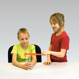 Auf dem Bild führen zwei Kinder ein Experiment durch. Ein Kind mit einem grünen T-Shirt misst mit einem roten Messgerät den Wasserstand in einem Glas, während das andere Kind aufmerksam zuschaut.