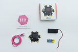 Das Bild zeigt ein Calliope mini-Board in der Mitte, umgeben von einem USB-Kabel, einer Batteriehalterung mit Batterien und einer Schnellstart-Anleitung. Der Artikel scheint für Bildungszwecke gedacht zu sein und fördert das Experimentieren mit Elektronik.
