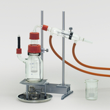 Das Bild zeigt eine chemische Apparatur, bestehend aus einem Glasbehälter, Schläuchen und einem Heizgerät, die für Experimente im Bildungswesen verwendet wird. Die Apparatur dient wahrscheinlich zur Destillation oder ähnlichen Experimenten in der Chemie.