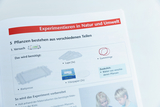 Das Bild zeigt eine Anleitung für ein Experiment über Pflanzen, das verschiedene Materialien auflistet, die dafür benötigt werden, darunter Lupen, Gummiringe und Filterpapier. Zusätzlich werden Blätter von verschiedenen Pflanzen als weiteres Material aufgeführt.