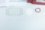 Das Bild zeigt verschiedene experimentelle Materialien, darunter eine transparente Box, mehrere Mikrolinsen sowie zwei weiße Folien und ein Gummiband. Diese Utensilien könnten für wissenschaftliche Experimente im Bildungsbereich verwendet werden.