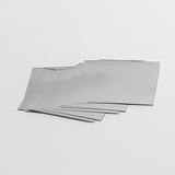 Das Bild zeigt eine Reihe von quadratischen, metallischen Platten, die auf einem weißen Untergrund liegen. Sie scheinen Teil eines Experimentierkits zu sein, das im Rahmen von Bildungszwecken verwendet wird.