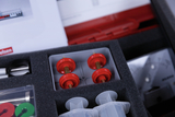 Das Bild zeigt eine Auswahl an Experimentiermaterialien, darunter rote Gewichte, transparente Spritzen und ein Messgerät. Die Teile sind ordentlich in einer gepolsterten Box angeordnet, die für den Bildungsbereich konzipiert ist.