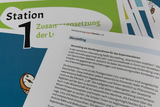 Das Bild zeigt Materialien für ein Experimentierraum-Konzept, das sich mit dem Thema Luft beschäftigt. Auf einem Arbeitsblatt wird das Konzept des Storytellings als Lehr- und Lernmethode erläutert, um das Verständnis für naturwissenschaftliche Phänomene zu fördern.