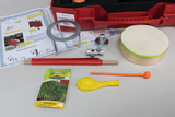 Das Bild zeigt ein Experimentier-Set mit verschiedenen Materialien wie einer Trommel, einem Kressesamenpacket, mehreren Röhren, einem Ballon und einer Anleitung zur Durchführung von Experimenten mit Luft. Alles ist in einem roten Koffer angeordnet, der für Bildungszwecke konzipiert ist.