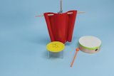 Das Bild zeigt verschiedene Experimentiermaterialien, darunter einen roten Vorhang, einen gelben Tisch mit etwas darauf und eine große Trommel mit einem orangefarbenen Schlagstock. Diese Utensilien könnten für verschiedene Bildungs- oder Experimentieraktivitäten im Unterricht genutzt werden.