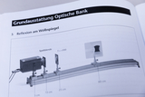 Das Bild zeigt eine schematische Darstellung einer optischen Bank zur Durchführung des Experiments zur Reflektion an einem Wölbspiegel. Es sind verschiedene Komponenten wie eine Spaltblende, ein Wölbspiegel und Messmarkierungen auf der Bank abgebildet.