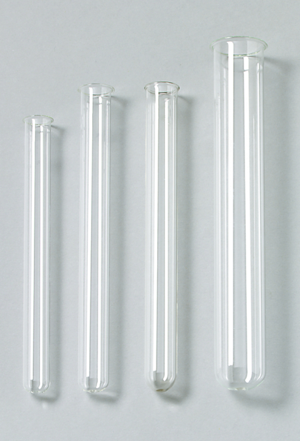 Das Bild zeigt vier transparente Reagenzgläser unterschiedlicher Länge, die nebeneinander angeordnet sind. Sie sind aus Glas gefertigt und haben eine gleichmäßige Form, die für chemische Experimente im Bildungswesen geeignet ist.