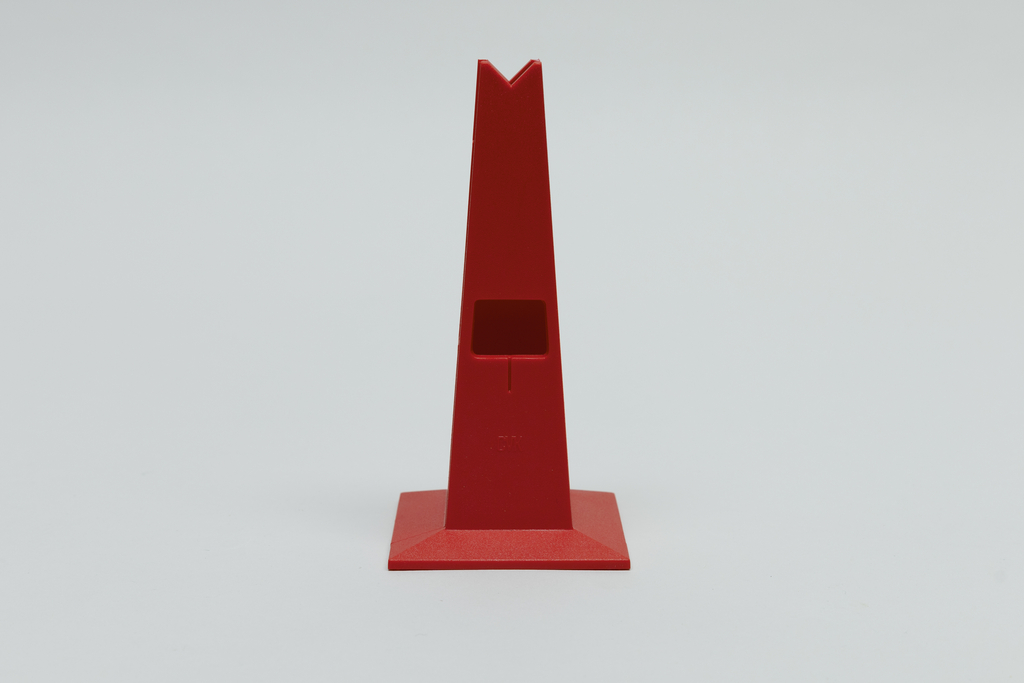 Das Bild zeigt einen roten, pyramidenförmigen Halter mit einer quadratischen Basis und einer Aussparung an der Vorderseite. Dieses Objekt könnte zur Befestigung oder Präsentation von Experimentiermaterialien im Bildungsbereich verwendet werden.