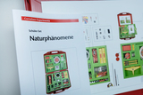 Das Bild zeigt eine Broschüre für ein Schüler-Set namens "Naturphänomene" aus dem Online-Shop für Experimentierbedarf. Neben der Broschüre ist eine Übersicht des Experimentier-Kits zu sehen, das verschiedene Materialien und Werkzeuge enthält.