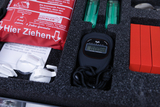 Das Bild zeigt einen Koffer mit Experimentiermaterialien, der Schutzbrillen, einen Stoppuhr und zwei grüne Reagenzgläser enthält. Zusätzlich ist ein rotes Notfallutensil zur Brandbekämpfung sowie Anweisungen im Inneren des Koffers zu sehen.