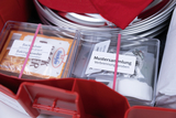 Das Bild zeigt ein Experimentierkit mit verschiedenen Materialien, darunter Backpulver und eine Mustersammlung für Verbrennungstests. Die Verpackungen sind ordentlich beschriftet und in einem roten Behälter angeordnet, der für Bildungszwecke gedacht ist.