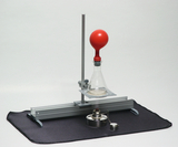 Das Bild zeigt ein Experimentiergerät, das eine Glasflasche mit einem roten Ballon und einer Heizquelle auf einer stabilen Plattform umfasst. Die Anordnung ist auf einem schwarzen Untergrund platziert und eignet sich für Experimente im Bildungsbereich.