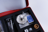 Das Bild zeigt ein Experimentier-Kit, das eine Vielzahl von Laborausrüstungen enthält, darunter einen kleinen Brenner, ein Glasgefäß und eine Schachtel mit Zündhölzern. Die Komponenten sind ordentlich in einem gepolsterten Behälter angeordnet, der einen einfachen Transport ermöglicht.