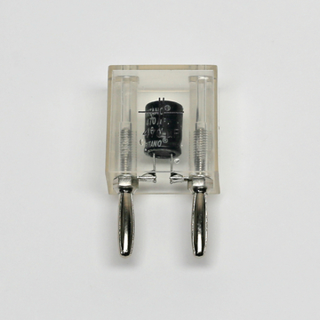 Das Bild zeigt einen transparenten Gehäuse mit einem Kondensator, der in der Mitte eingelassen ist. An beiden Seiten befinden sich Metallkontakte zur Verbindung mit einem Stromkreis, ideal für Experimente im Bildungsbereich.