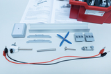 Das Bild zeigt diverse Komponenten eines Experimentierkits zur Energieumwandlung, darunter Motoren, eine Propellerblatte, Verbindungselemente und ein Anleitungsheft. Alle Teile sind übersichtlich angeordnet und in einer roten Aufbewahrungsbox untergebracht.