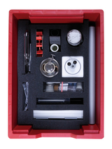 Das Bild zeigt eine rote Box, die mit verschiedenen Experimentiermaterialien ausgestattet ist, darunter Glasgeräte, eine Spritze, und diverse kleine Behälter. Alle Utensilien sind sicher in Schaumstoff eingelegt, um sie während des Transports zu schützen.