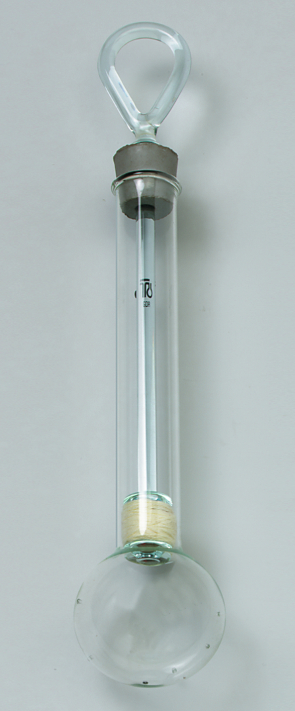 Das Bild zeigt einen Experimentierglasartikel, der aus einem langgestreckten Glasrohr mit einer halbkugelförmigen Basis besteht. Oben hat es einen geschlossenen Hals, der eine Aufhängemöglichkeit bietet, und im Inneren sind Materialien sichtbar, die für chemische Experimente genutzt werden können.