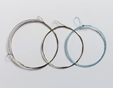 Das Bild zeigt drei verschiedene Drahtringe, die für experimentelle Zwecke im Bildungswesen verwendet werden können. Die Ringe variieren in Größe und Material, wobei einer aus blauem Draht und die anderen aus silbernem Draht bestehen.