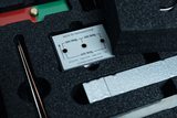 Das Bild zeigt eine Vorrichtung mit einer Plakette, die technische Spezifikationen für elektrische Experimente enthält. Sie befindet sich in einem schaumstoffgepolsterten Behälter, der wohl für den sicheren Transport und die Aufbewahrung gedacht ist.