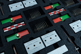 Das Bild zeigt ein Set von Experimentiermaterialien, das in einem schaumstoffgepolsterten Behälter angeordnet ist. Es enthält verschiedene Komponenten wie Federkontakte, Leitungen und Bauteile mit Beschriftungen, die unterschiedliche Werte anzeigen.