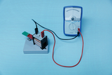 Das Bild zeigt ein Experimentiergerät mit einer Spule, einem Schalter und einem Galvanometer, das zur Messung von elektrischen Strömen verwendet wird. Die Anordnung dient vermutlich zur Demonstration von elektromagnetischen Effekten im Bildungsbereich.