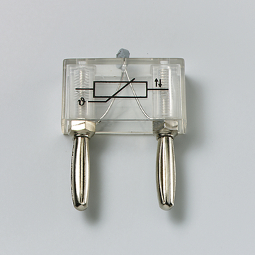 Das Bild zeigt ein transparentes Gerät mit zwei silbernen Anschlüssen und einem einfachen Schaltkreis in der Mitte. Es ist wahrscheinlich ein Experimentiergerät zur Demonstration von elektrischen oder physikalischen Prinzipien im Bildungsbereich.