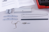 Das Bild zeigt verschiedene Experimentiermaterialien, darunter Halterungen, Ketten und ein graues Rohr, die möglicherweise für physikalische oder technische Experimente gedacht sind. Neben den Materialien liegt ein Handbuch mit Anweisungen auf einem weißen Hintergrund.