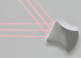 Das Bild zeigt eine gebogene Linse vor einer hellen Fläche, auf der mehrere rote Laserstrahlen sichtbar sind. Die Strahlen verlaufen parallel und verdeutlichen die optischen Eigenschaften der Linse in einem experimentellen Kontext.