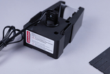 Das Bild zeigt ein elektrisches Bauteil mit einer Anschlussklemme und einem Warnhinweis bezüglich der Lampentemperatur. Neben dem Gerät liegen mehrere schwarze Streifen, die vermutlich für ein Experiment verwendet werden.
