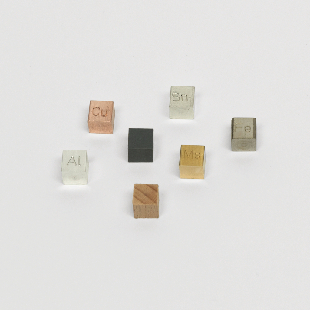 Das Bild zeigt eine Sammlung von Würfeln aus verschiedenen Materialien, die mit chemischen Symbolen geprägt sind. Diese Stoffe, darunter Aluminium (Al), Kupfer (Cu) und Zinn (Sn), dienen Bildungszwecken im Experimentierbereich.