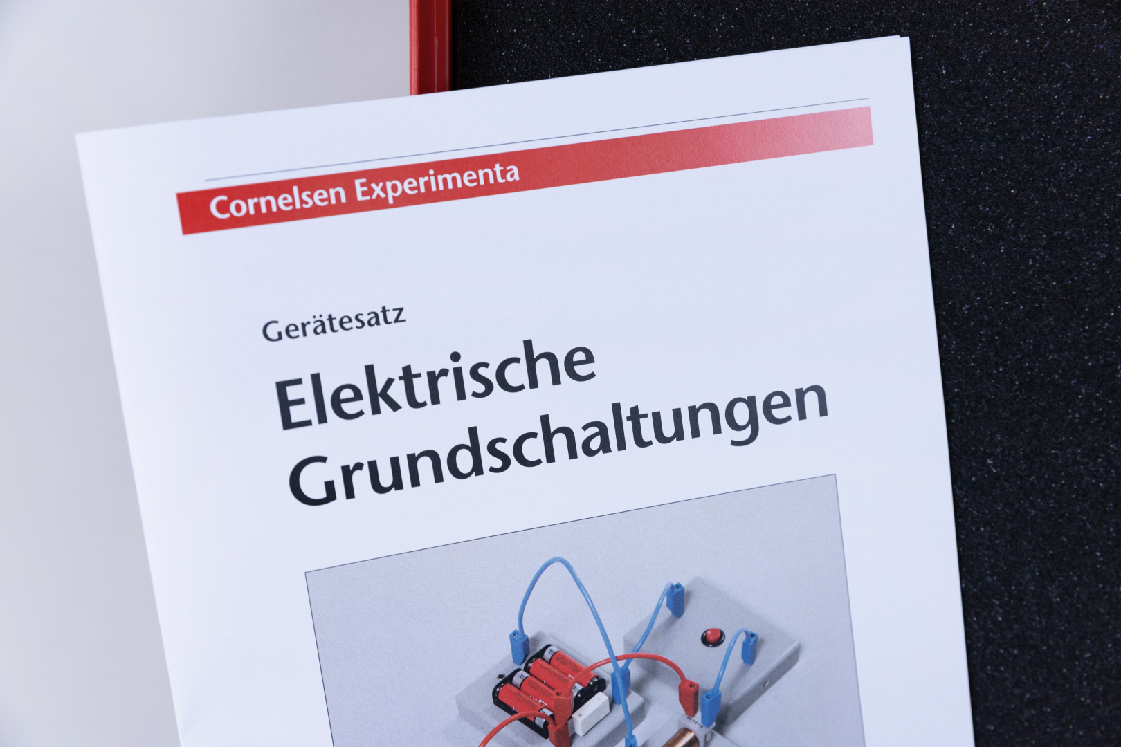 Das Bild zeigt ein Handbuch mit dem Titel „Elektrische Grundschaltungen“ aus dem Cornelsen Experimenta Shop. Auf dem Cover ist ein experimenteller Schaltkreis abgebildet, der für den Unterricht im Bereich Elektronik verwendet werden kann.