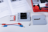 Das Bild zeigt verschiedene Komponenten eines Experimentiersets, darunter eine Batteriehalterung, Kabelverbinder und eine Glühbirne. Zudem sind ein Handbuch und weitere Teile in einem roten Koffer zu sehen, die für Bildungszwecke in der Naturwissenschaft verwendet werden können.