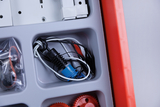 Das Bild zeigt eine Übersicht von verschiedenen Komponenten in einem Experimentierkasten, darunter Kabel, Stecker und Zahnräder, die für technische oder elektrische Experimente verwendet werden können. Die Teile sind ordentlich in einem grauen Fach angeordnet, das Teil eines roten Behälters ist.