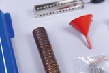 Das Bild zeigt verschiedene Laborinstrumente, darunter einen roten Trichter, ein metallisches Werkzeug mit Löchern und einen zylinderförmigen, braunen Gummiartikel mit Struktur. Diese Utensilien sind für experimentelle Tätigkeiten im Bildungsbereich geeignet.