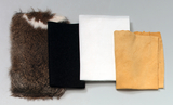 Das Bild zeigt eine Anordnung von verschiedenen Stoffen, darunter Pelz, schwarzer Filz, weißer Stoff und gelbes Leder. Diese Materialien könnten für experimentelle Projekte im Bildungsbereich verwendet werden.
