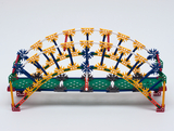 Das Bild zeigt eine Modellbrücke aus bunten Konstruktionsbausteinen, die in einem experimentellen Lern-Setting verwendet wird. Die Brücke ist gewölbt und demonstriert Prinzipien des Bauingenieurwesens und der Statik für Schüler.