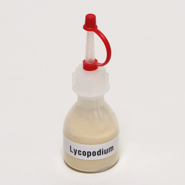 Das Bild zeigt eine Flasche mit Lycopodium, die einen gelblichen Inhalt hat und mit einem roten Spritzverschluss versehen ist. Die Verpackung ist klar beschriftet und wirkt aufgeräumt, ideal für den Einsatz im Bildungsbereich.
