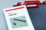 Das Bild zeigt eine Anleitung für ein Schüler-Set zum Thema "Solarzelle" von Cornelsen Experimenti. Abgebildet sind mehrere Solarzellen mit angeschlossenen Drähten und einem kleinen Motor, die zur Durchführung von Experimenten im Bildungsbereich gedacht sind.
