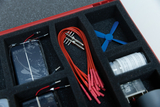 Das Bild zeigt eine Auswahl an Experimentiermaterialien, die in einem roten Koffer angeordnet sind. Zu den enthaltenen Artikeln gehören Solarpanels, rote Verbindungskabel, ein kleiner Propeller und weitere Komponenten für wissenschaftliche Experimente.