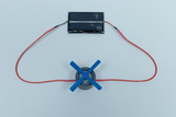 Das Bild zeigt ein einfaches Experimentier-Setup, bestehend aus einem kleinen Motor mit blauen Propellern, der mit einem Solarzellenmodul verbunden ist. Diese Anordnung demonstriert, wie Sonnenlicht in mechanische Energie umgewandelt werden kann.