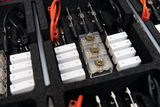 Das Bild zeigt ein vielfältiges Set von Experimentierzubehör, das in einer gepolsterten Box angeordnet ist. Zu sehen sind verschiedene Adapter, Kabel, sowie transparente und weiße Bauteile, die für Bildungszwecke im naturwissenschaftlichen Unterricht verwendet werden.