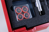 Das Bild zeigt eine rote Aufbewahrungsbox, die mit Schaumstoff ausgekleidet ist und verschiedene Experimentiermaterialien enthält. Besonders auffällig sind die vier roten Kompasse, die ordentlich in einer transparenten Verpackung angeordnet sind.