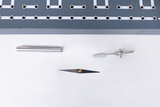 Das Bild zeigt eine Auswahl von Experimentiermaterialien, darunter einen metallischen Stab, ein dünnes Blatt und ein weiteres technisches Bauteil. Diese Objekte sind auf einem weißen Hintergrund angeordnet, wobei im Hintergrund ein graues Element mit Löchern und Linien zu sehen ist.