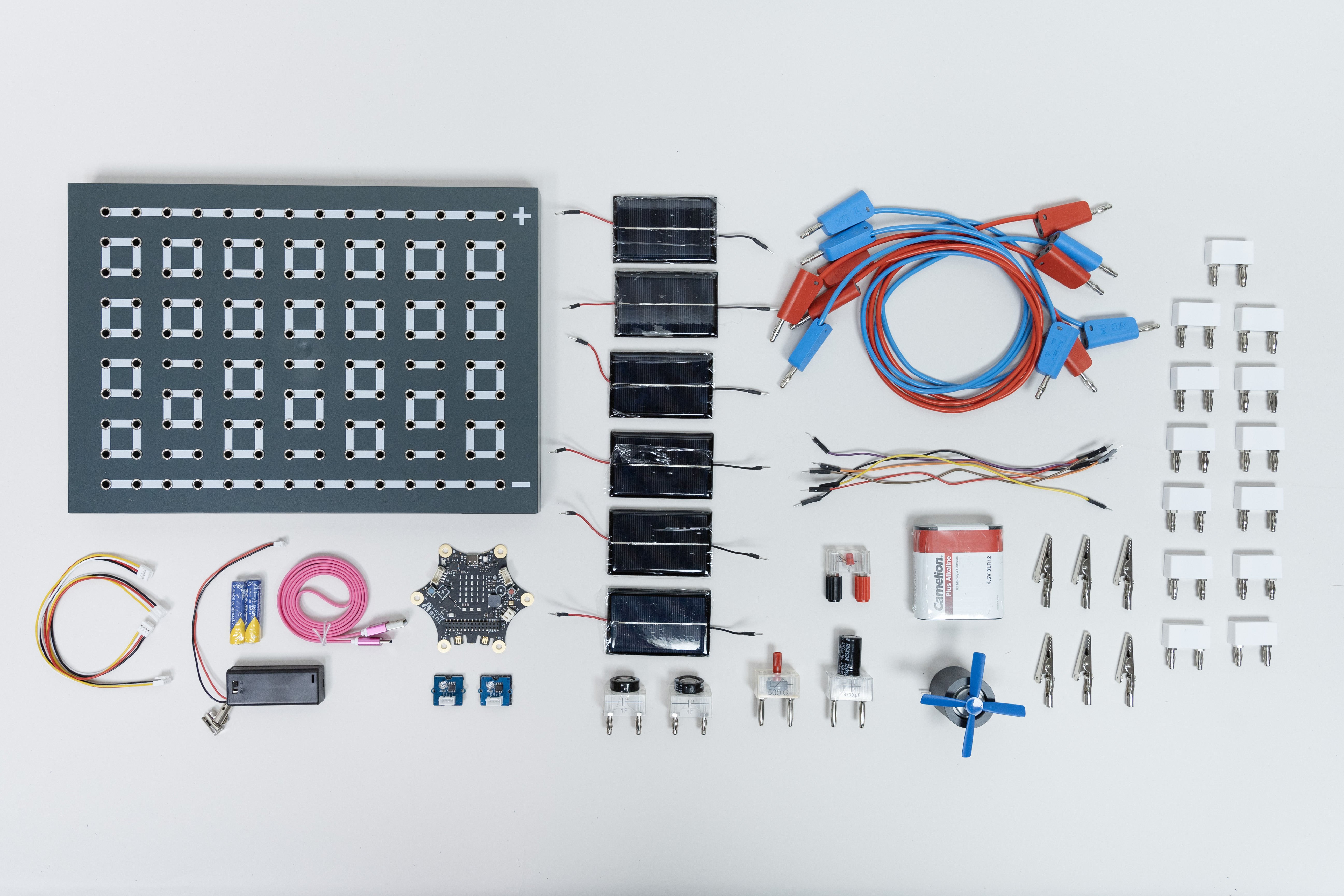 Das Bild zeigt eine Vielzahl von Experimentiermaterialien, darunter eine Leiterplatte mit Schaltern, Solarzellen, Kabel, elektrische Bauteile und Anschlüsse. Diese Komponenten sind für Lehr- und Lernzwecke im Bereich Technik und Naturwissenschaften konzipiert.