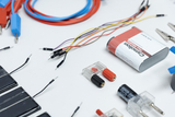 Das Bild zeigt eine Vielzahl von Experimentiermaterialien wie Kabel, Widerstände, Solarzellen und Batterien, die auf einem weißen Untergrund angeordnet sind. Diese Komponenten eignen sich ideal für praktische Anwendungen im Bildungsbereich, insbesondere in der Naturwissenschaft.