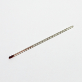 Das Bild zeigt ein Thermometer aus Glas mit einer roten Flüssigkeit, das zur Messung von Temperaturen verwendet wird. Es ist auf einer weißen Oberfläche platziert und besitzt eine Skala von 0 bis 100 Grad Celsius.