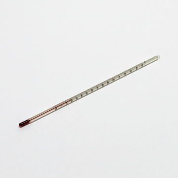 Das Bild zeigt ein Thermometer aus Glas mit einer roten Flüssigkeit, das zur Messung von Temperaturen verwendet wird. Es ist auf einer weißen Oberfläche platziert und besitzt eine Skala von 0 bis 100 Grad Celsius.